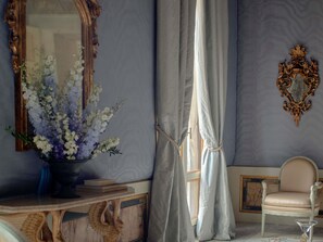Una habitación con un espejo, un florero, una silla y un adorno en la pared.