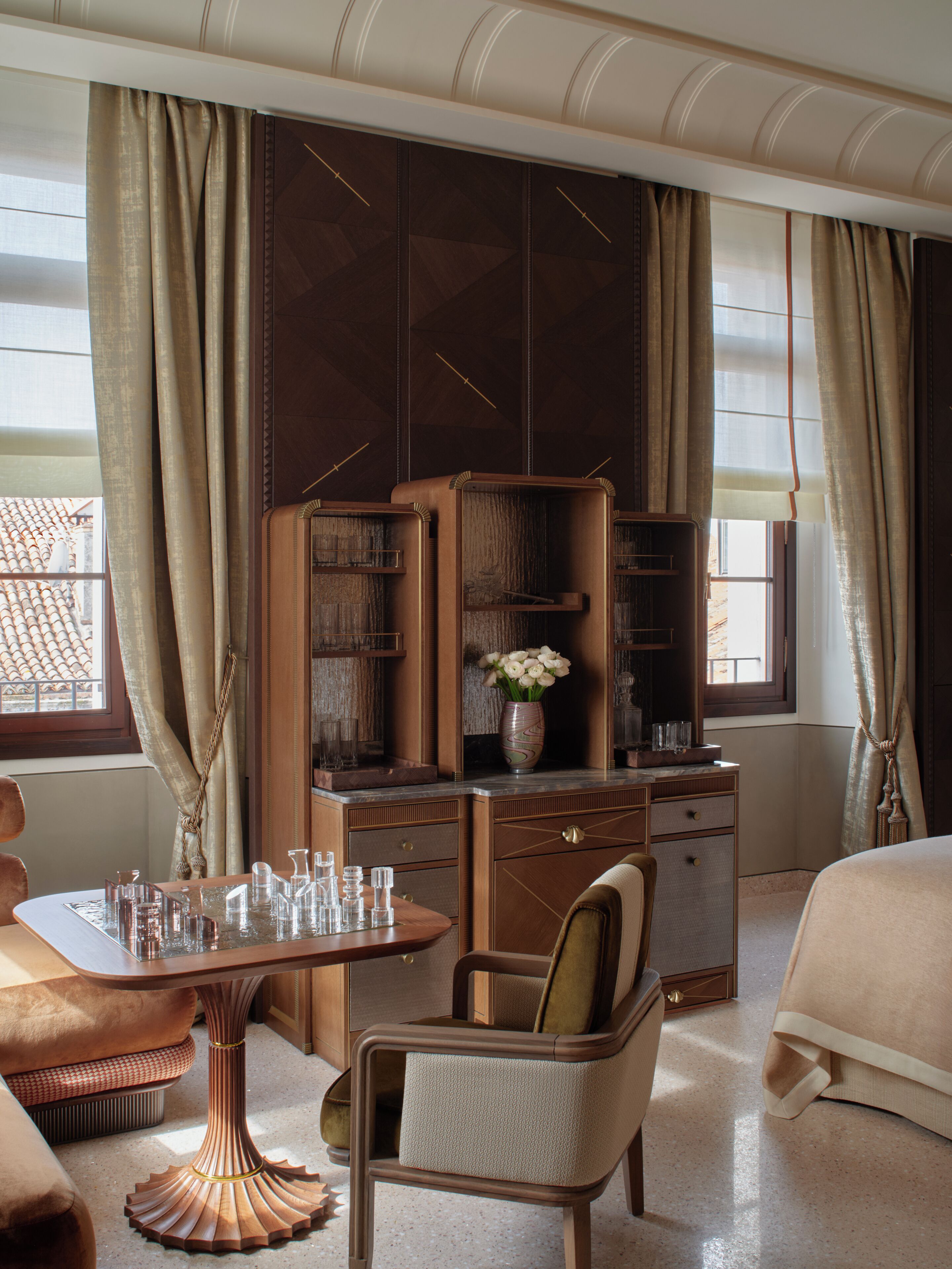 A hotel room with a bed, a desk with a chair, a vanity with a mirror, a dresser, and a window with curtains.
