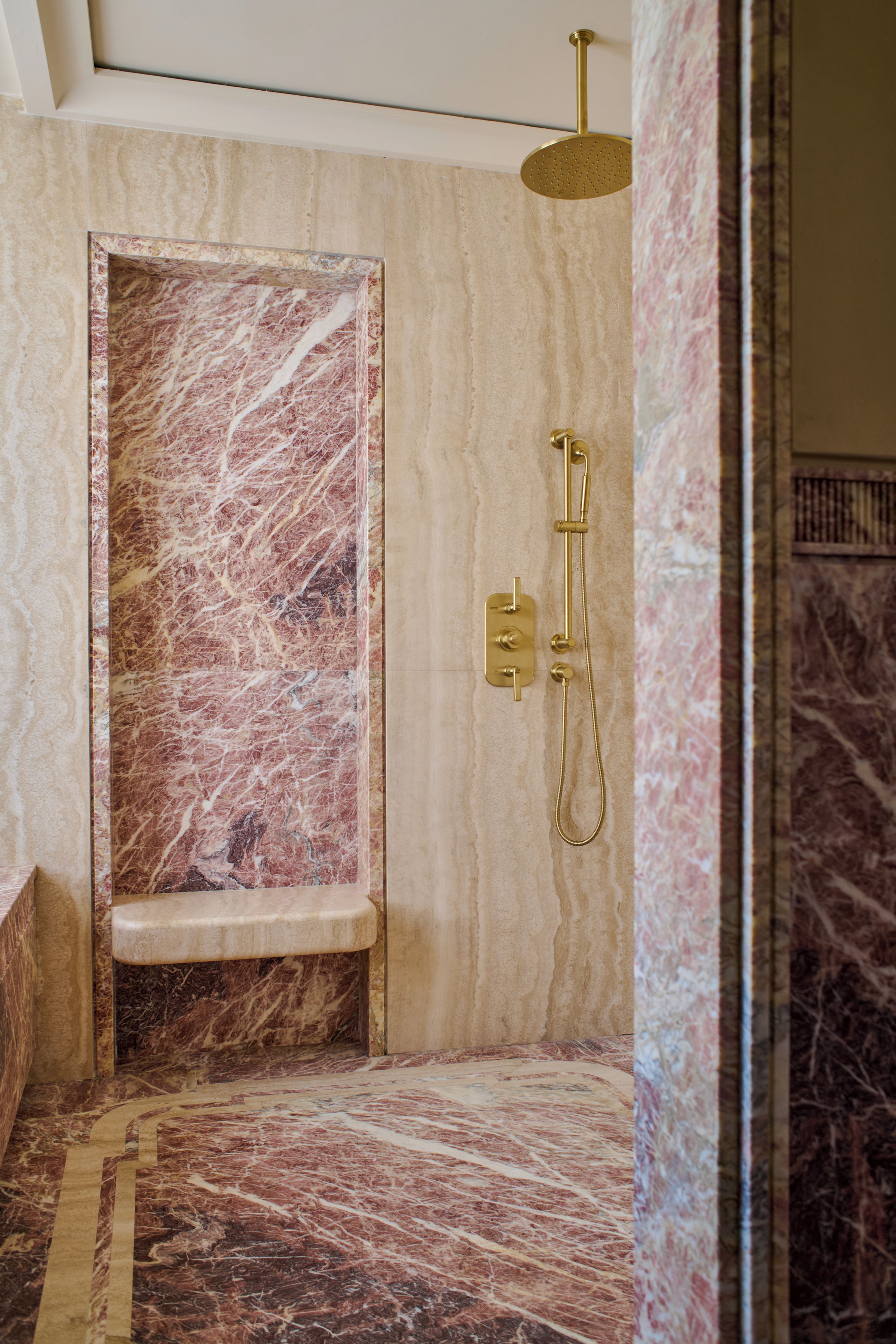 Une salle de bain avec un espace de douche en marbre, une pomme de douche dorée et un sol en marbre.