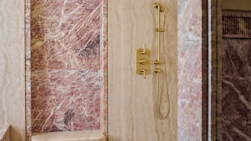 A bathroom with a marble shower enclosure, a gold showerhead, and a marble floor.