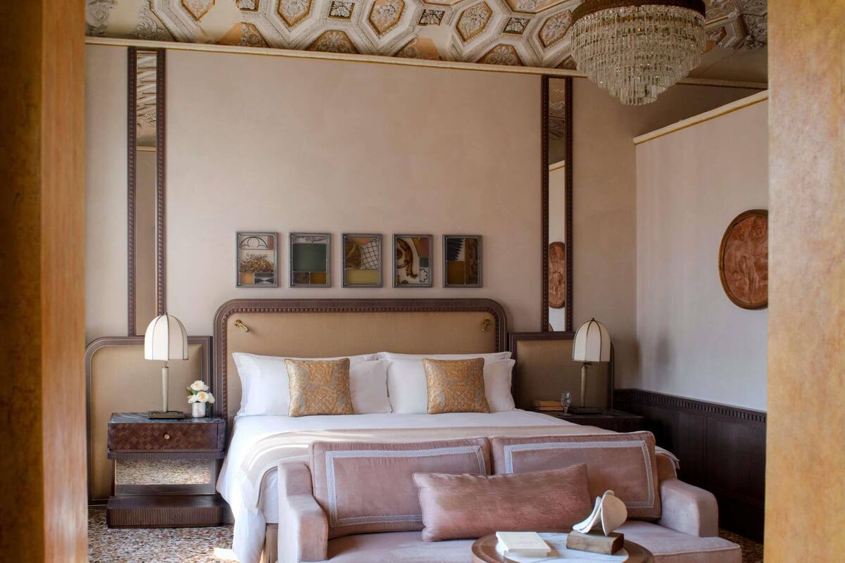 A hotel room with a large bed, a sofa, a small table, and a chandelier.