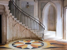 Una maestosa scalinata con ringhiere elaborate che conduce a un pianerottolo con pavimento decorato.