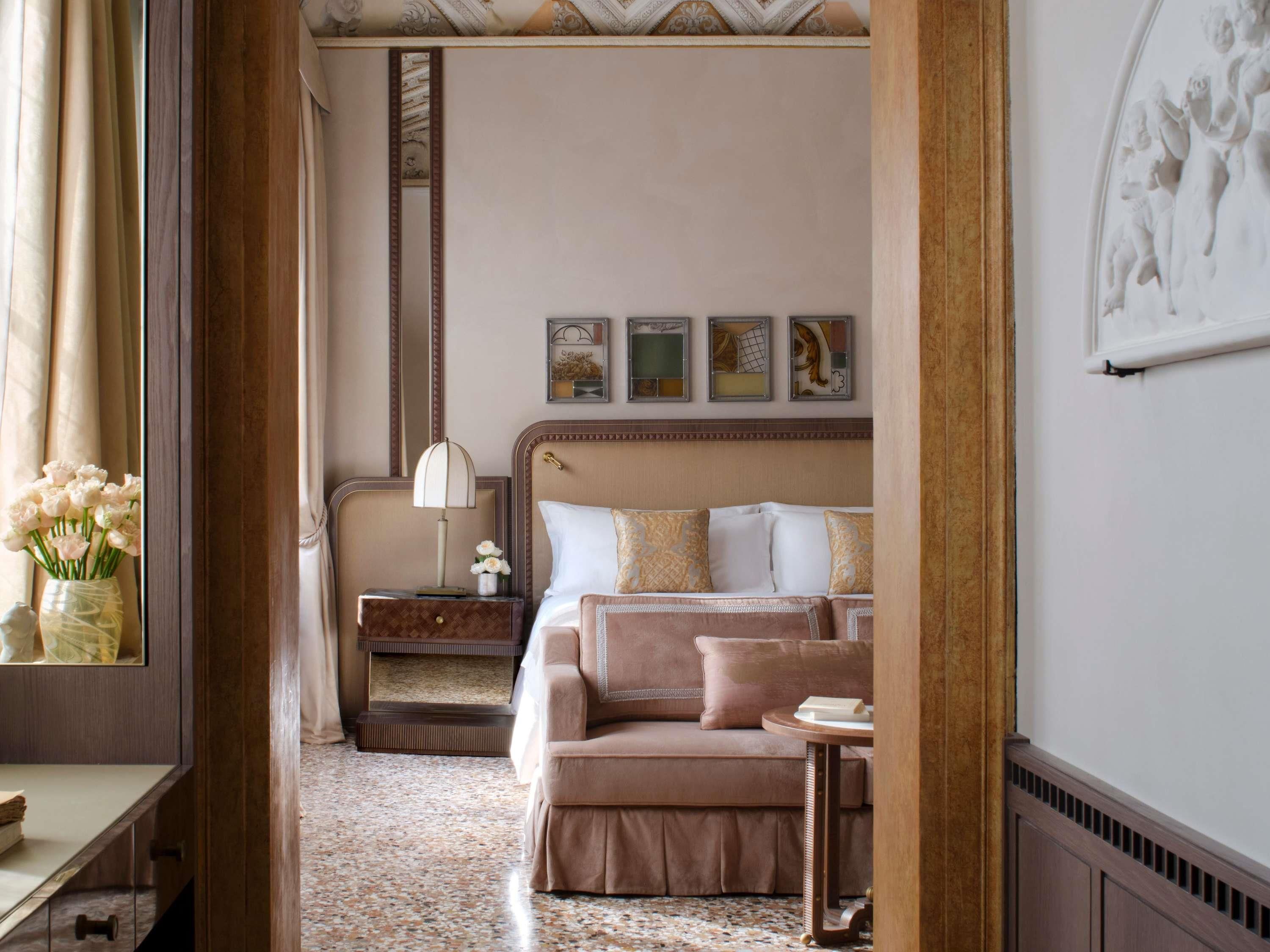 Une chambre d’hôtel avec un lit, une table de chevet, une lampe, un vase de fleurs et un tableau encadré au mur.