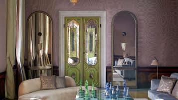 Una habitación con puerta verde, un sofá, una mesa de ajedrez y una araña.