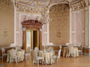 Un comedor opulento con decoraciones ornamentales en el techo, candelabros y muebles clásicos.