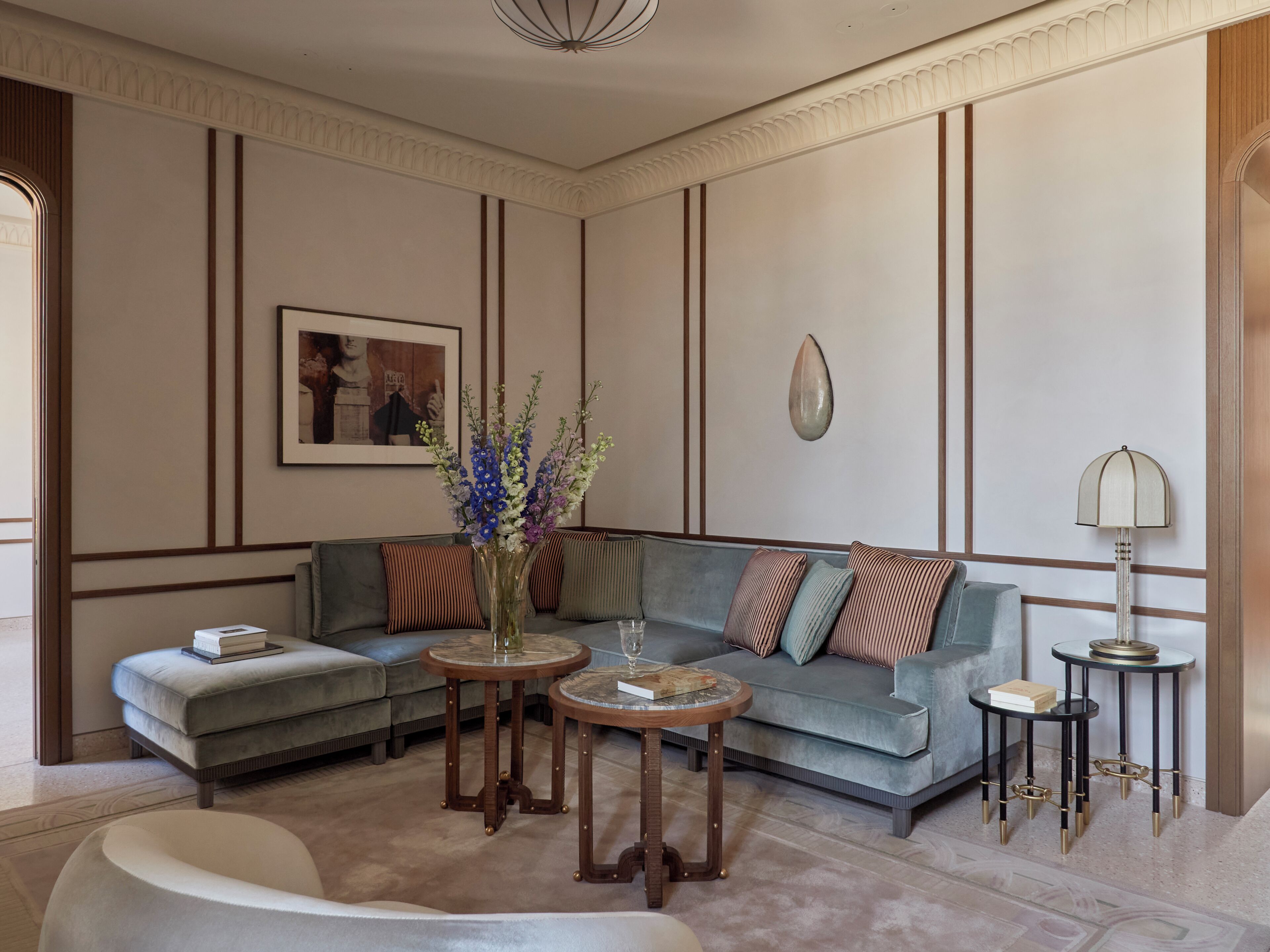 A modern living room with a sectional sofa, two round wooden tables, a floor lamp, and a framed picture on the wall.
