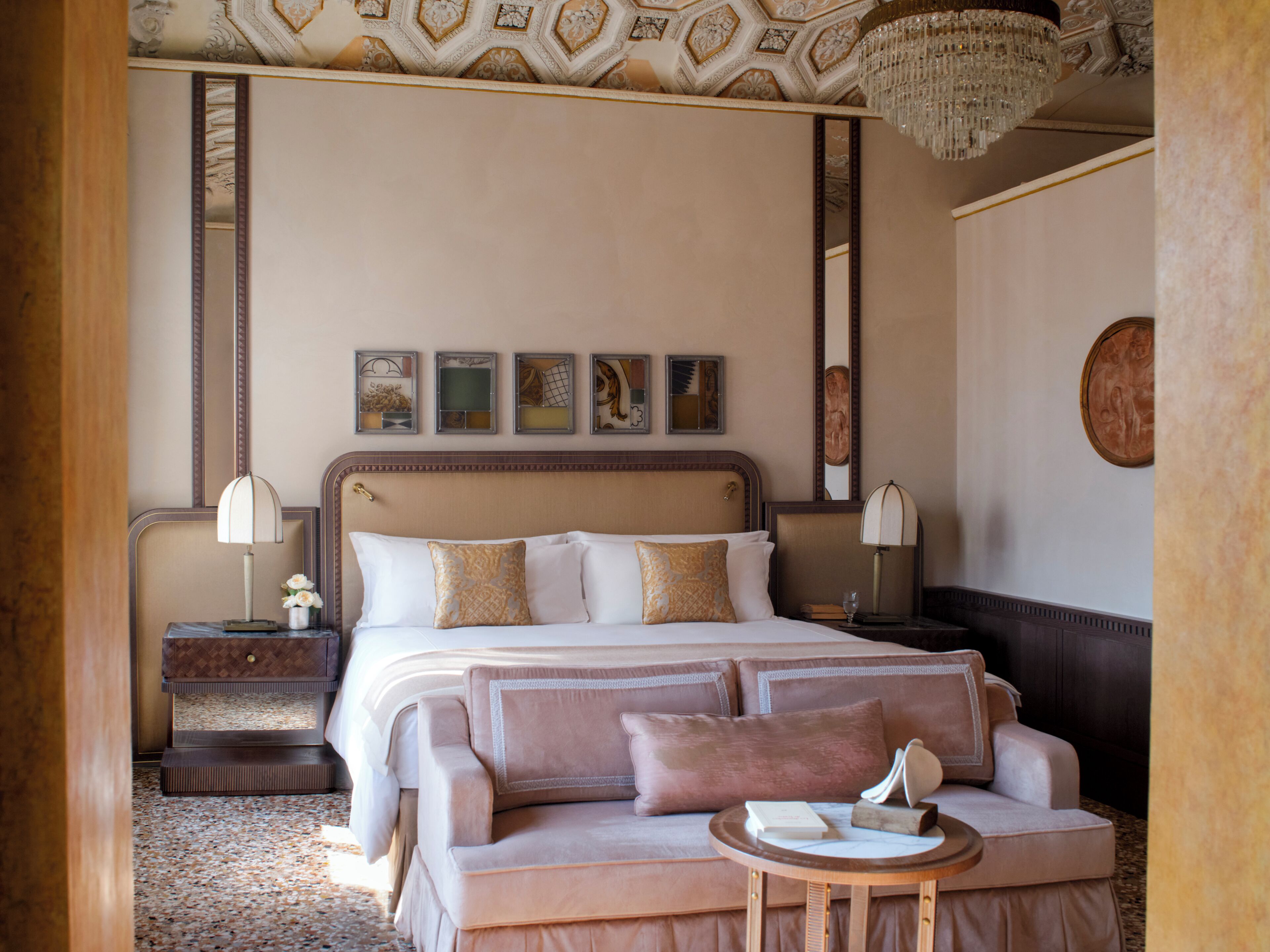 A hotel room with a large bed, a sofa, a small table, and a chandelier.