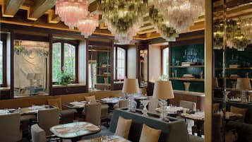 A restaurant interior with multiple dining tables, chairs, and hanging chandeliers.