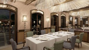 Un espace repas avec des tables dressées, des portes en arc de cercle et une vue sur la terrasse extérieure.