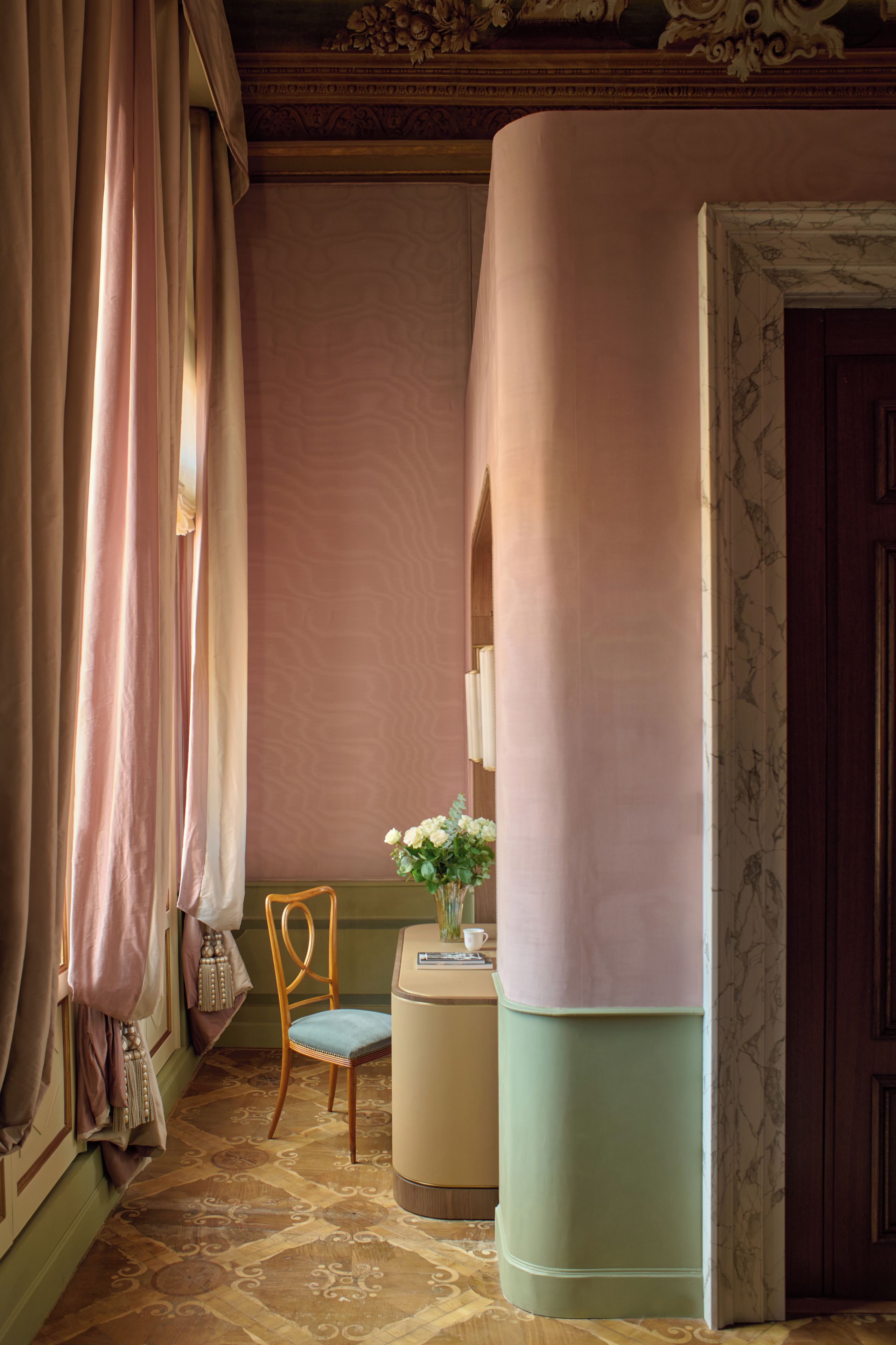 Una stanza con una sedia di legno, un tavolino con un vaso di fiori e una porta decorata con un motivo marmorizzato.