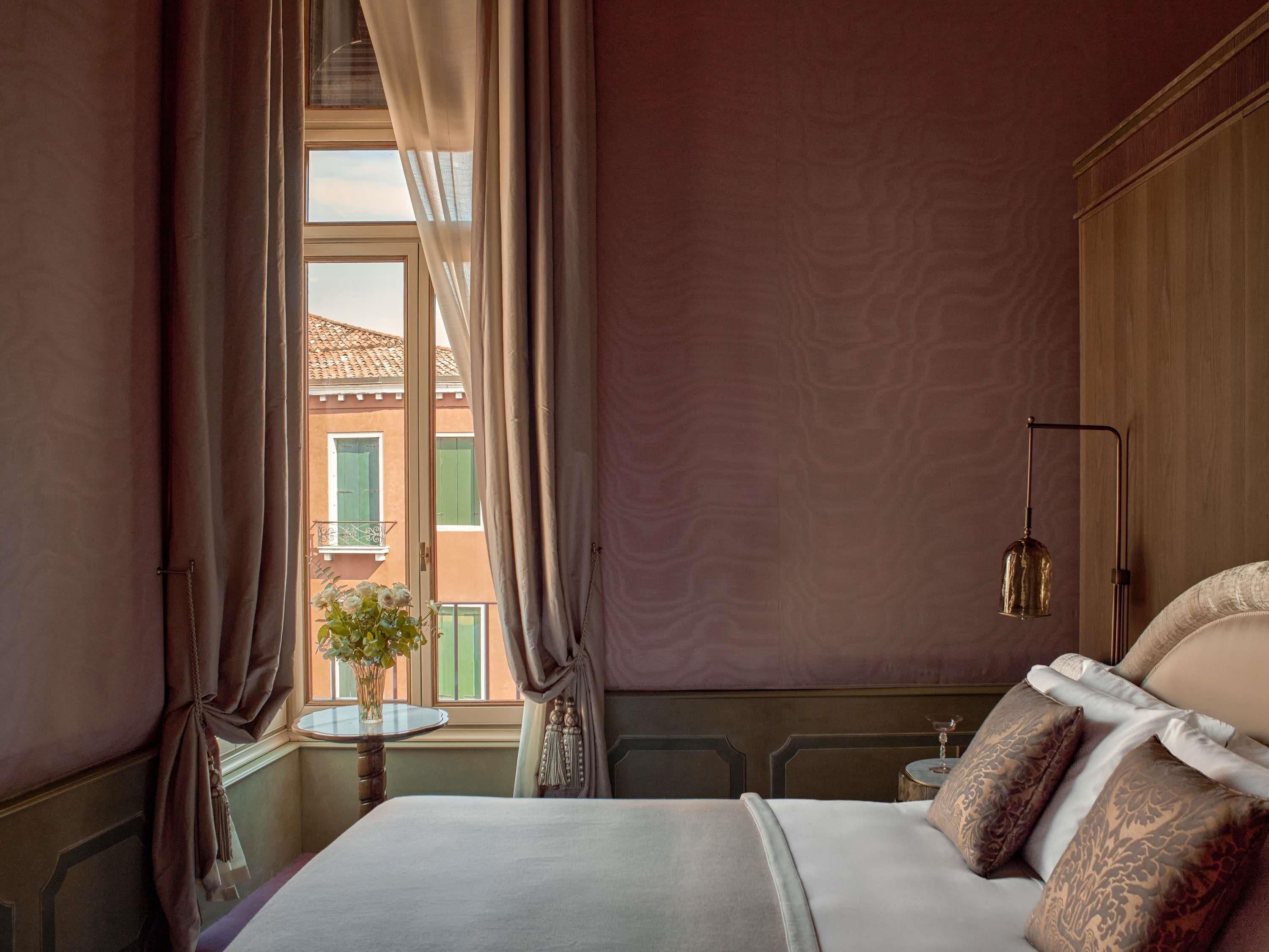 A bedroom with a bed, curtains, a window, a bedside table, and a lamp.