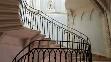 Eine imposante Treppe mit aufwendigen schwarzen Wangen, eine Statue im Hintergrund und klassische architektonische Details.