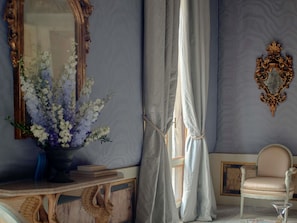 A room with a mirror, a vase of flowers, a chair, and a decorative wall piece. - Orient Express Venezia (Venice)