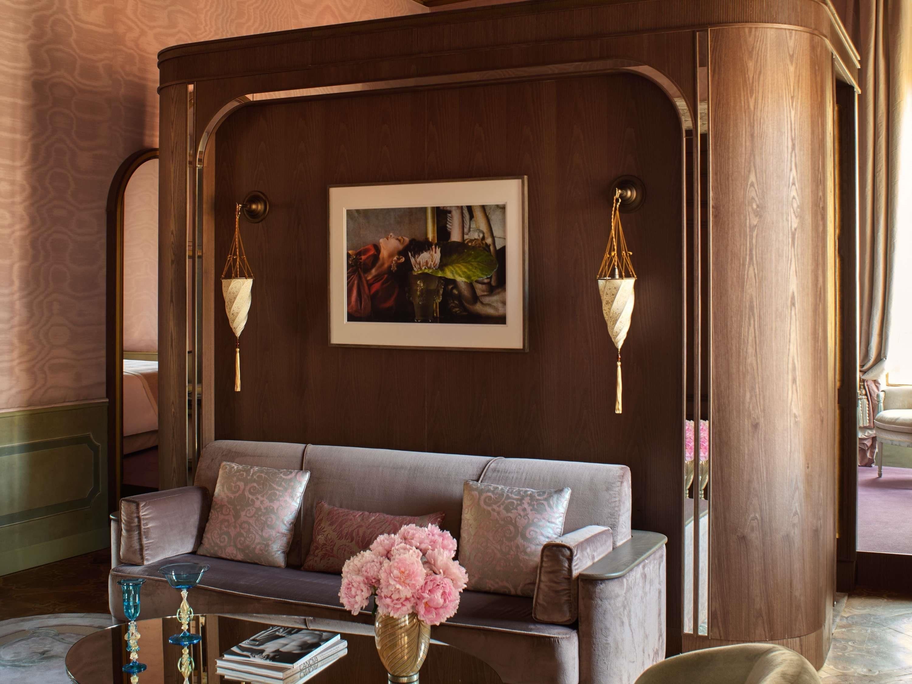 A room with a sofa, a framed artwork, and a vase with flowers.