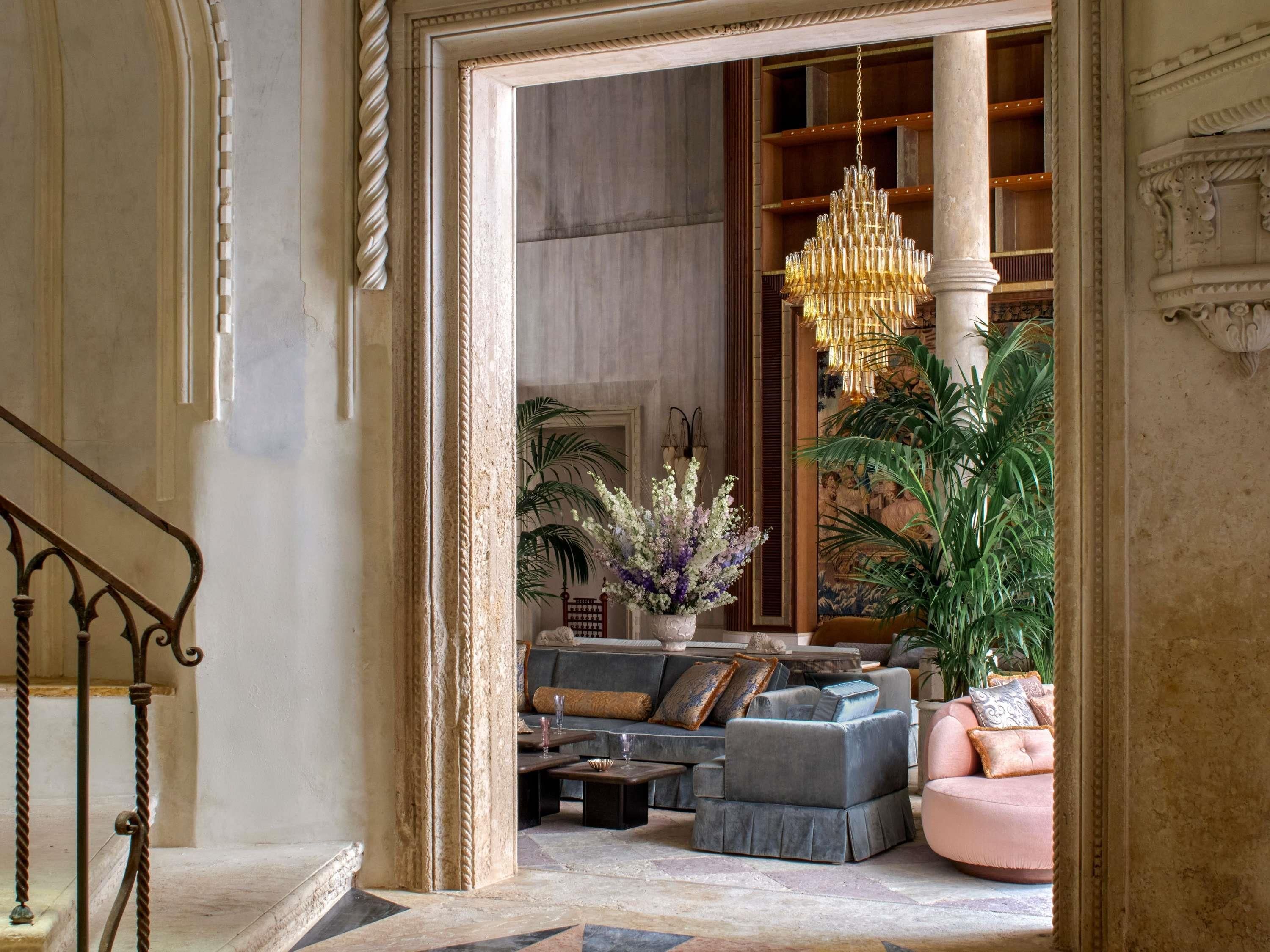 A grand lobby with a chandelier, sofas, a coffee table, and a staircase.