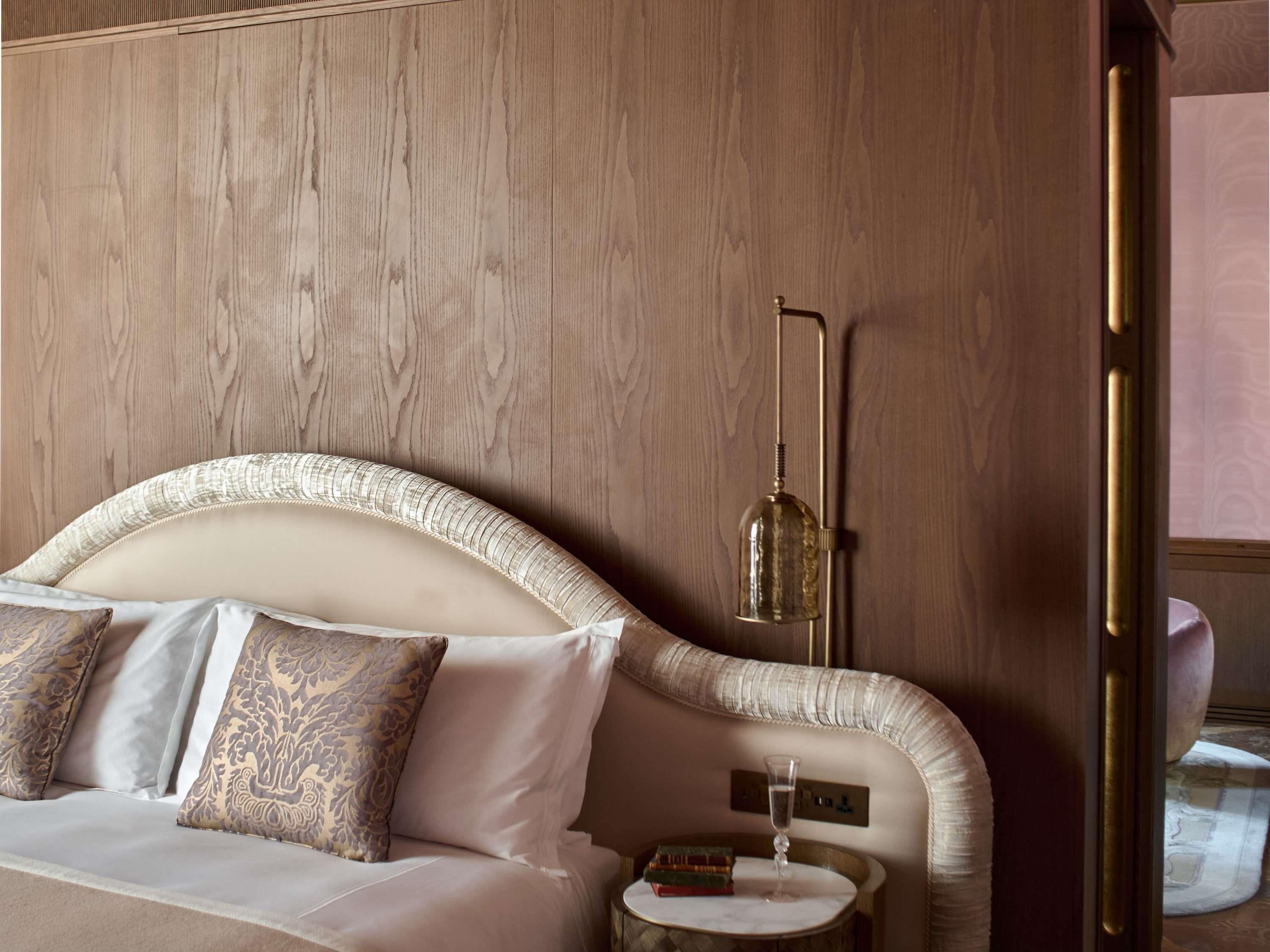 A hotel room with a curved headboard, a bedside table with a glass of water, and a lamp.