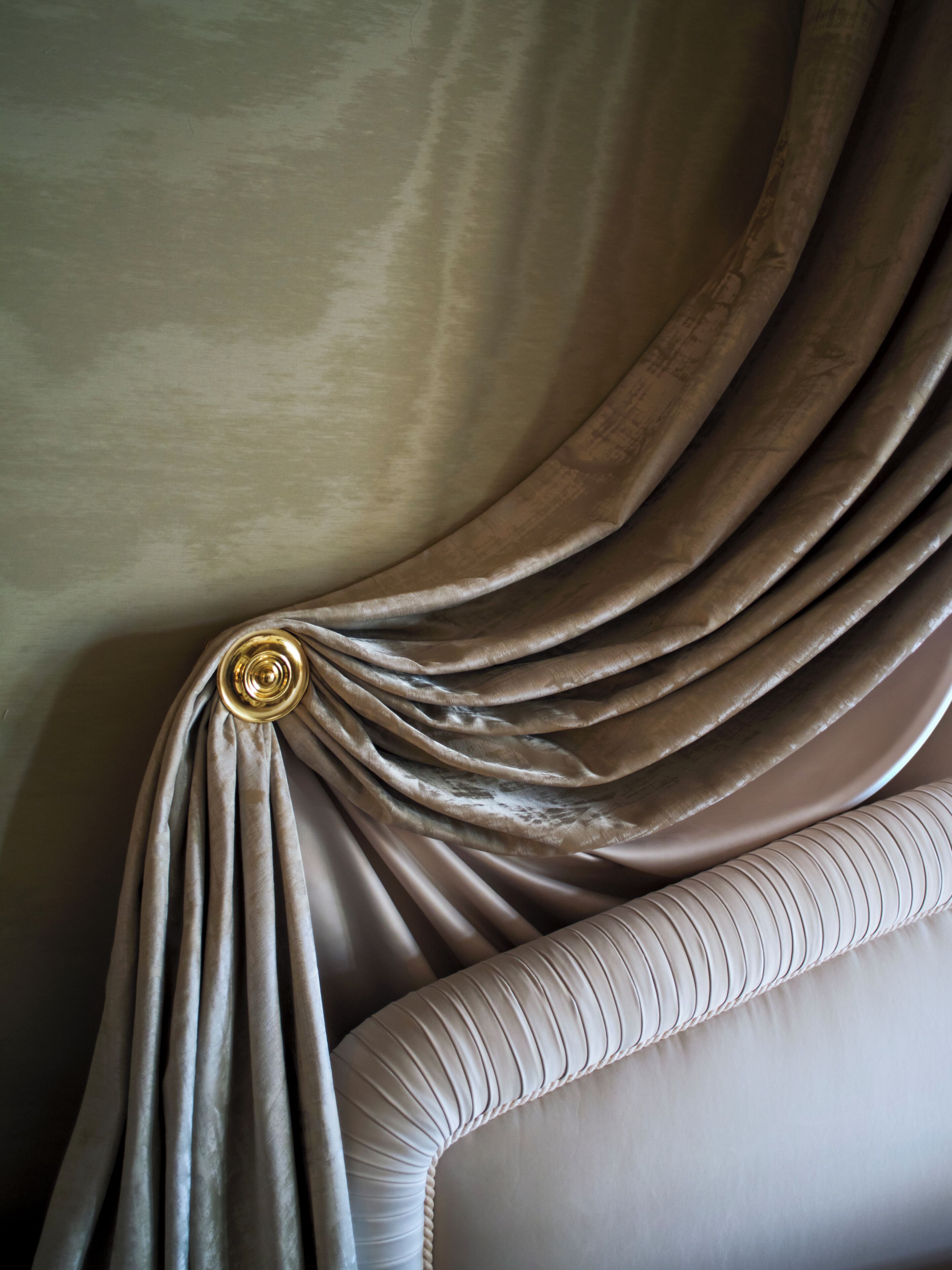 Un gros plan d’un tissu drapé, agrémenté d’un bouton métallique, d’une structure rembourrée aux lignes courbes et d’un mur à la texture particulière.
