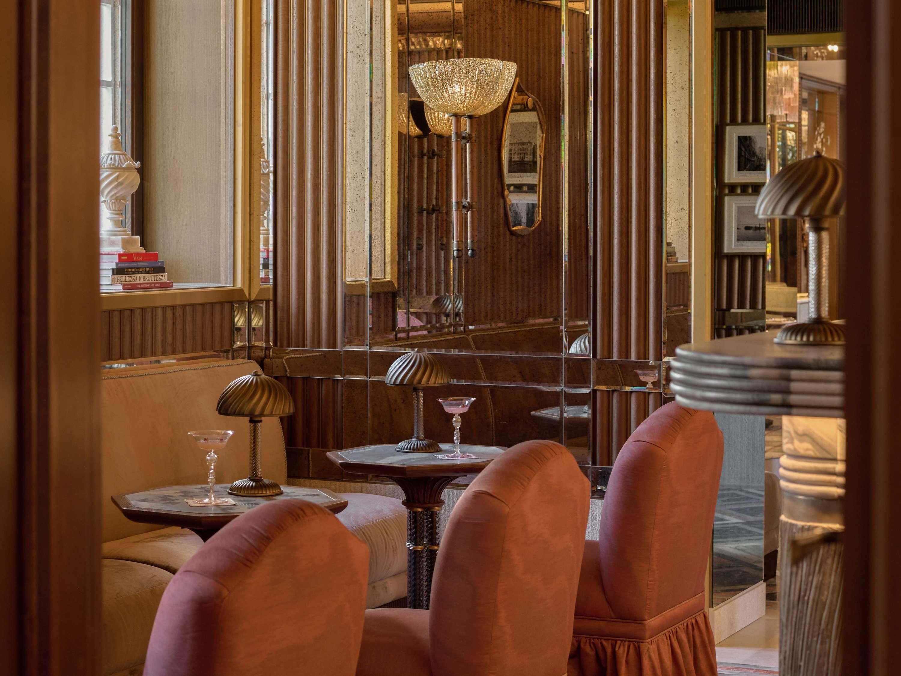 A room with a mirrored wall, a chandelier, and a table with a wine glass.