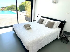 Ein modernes Schlafzimmer mit einem großen Bett, Blick auf ein Schwimmbecken und einem Balkon.