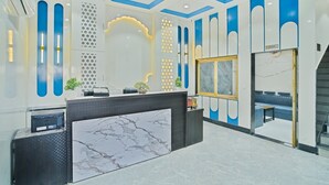 A modern reception area with a marble reception desk, a seating area with a sofa, and decorative wall patterns. - The Heritage Bagh (Luni)