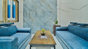 A modern lobby with a marble wall, blue sofas, a wooden coffee table with a plant, and a small wooden side table. - The Heritage Bagh (Luni)