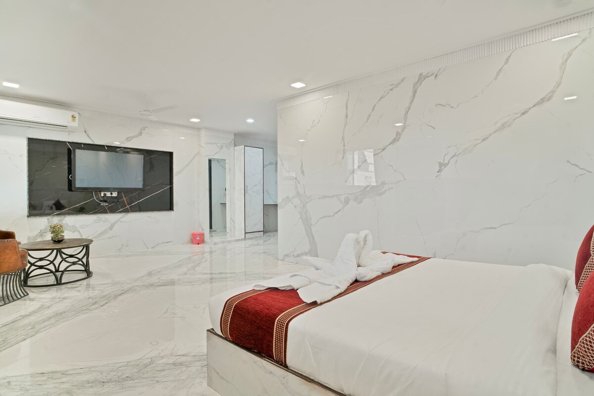 A modern hotel room with a large bed, a TV mounted on the wall, and a marble floor.