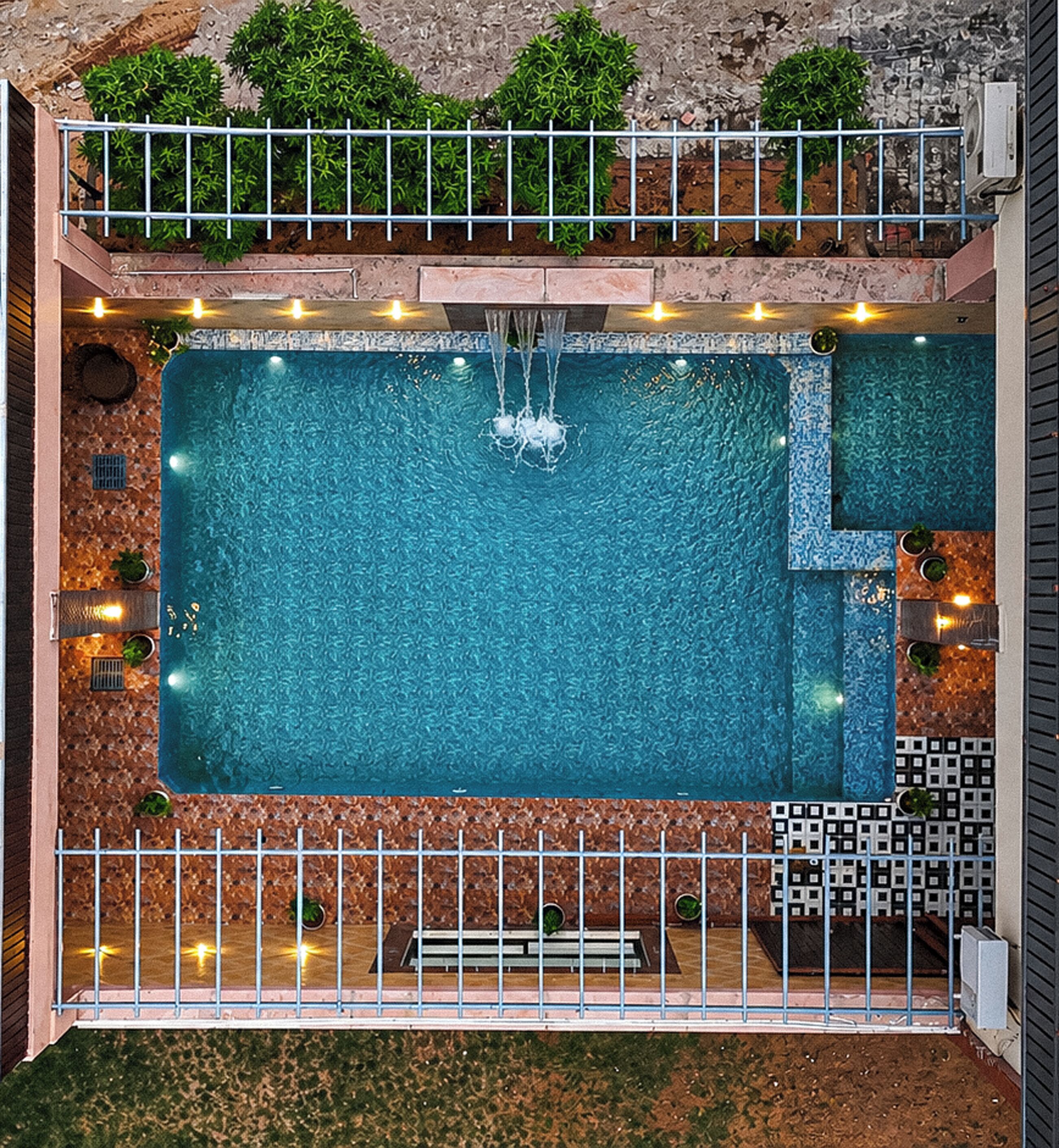 Piscina no terraço com vista clara do céu, cercada por uma grade de metal e uma pequena área ajardinada.