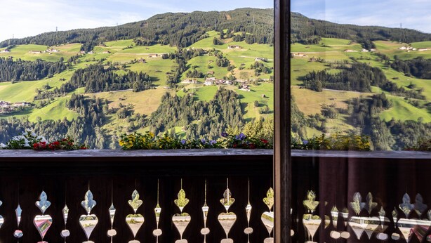 Uitzicht vanaf een balkon met houten balustrade, over een groen dal met verspreide gebouwen en bomen.