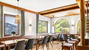 Een eetgedeelte met houten tafels en stoelen, grote ramen met uitzicht op het landschap, en een houten plafond.