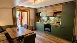 Een kleine keuken met houten kastjes, een ingebouwde oven, en een eethoek met een tafel en stoelen.