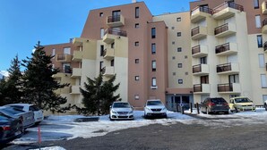 Un immeuble résidentiel à plusieurs étages, doté de balcons, avec des voitures garées et de la neige au sol.