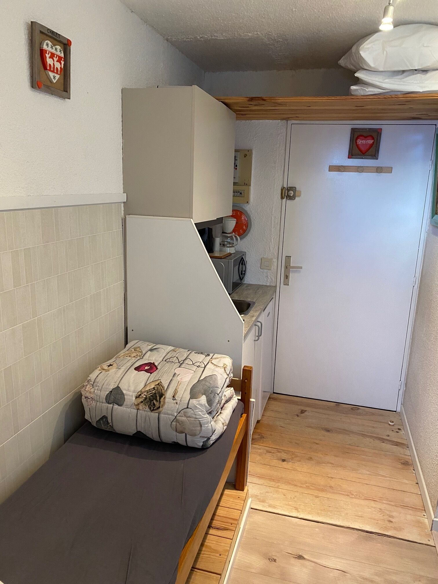 Une pièce de taille modeste comprenant un lit, un petit coin cuisine et une porte donnant sur une autre pièce.