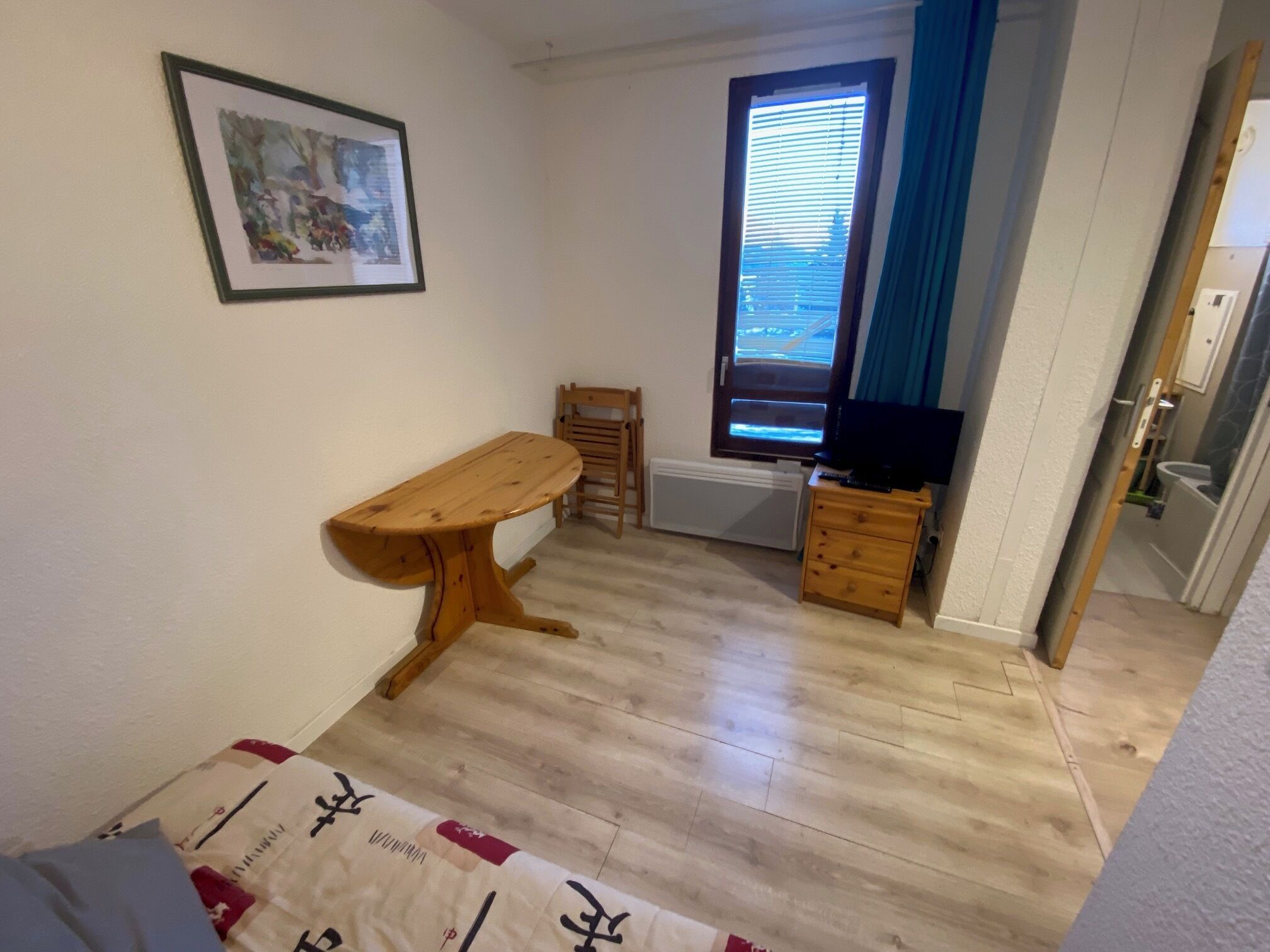 A small room with a wooden table, a chair, a television, and a window with blinds.