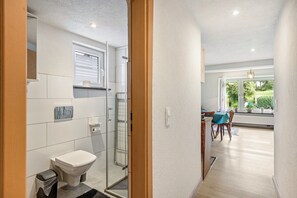 A modern bathroom with a toilet, shower, and glass door, leading to a dining area with a table and chairs.