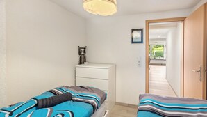 Een slaapkamer met twee bedden, een bureau en een deur naar een gang.