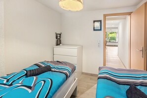 A bedroom with two beds, a desk, and a door leading to a hallway. - Apartment 'Jolie' with Mountain View, Private Terrace and Wi-Fi (Söhrewald)