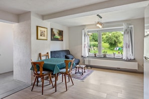 Een eetruimte met een tafel voor vier personen, een bank en een raam met uitzicht op groen.