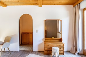 Een kamer met een houten garderobe, een spiegel, een klein krukje en een stoel.