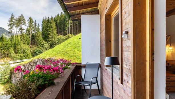 A wooden balcony with a chair, a small table, and a lamp.