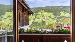 A wooden cabin with a balcony overlooking a valley with houses and greenery.
