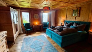 A wooden cabin interior with a bed, two chairs, a desk, and a large window. - Double Room 'Zirben Nest' with Stunning View and Private Floor Bathroom (Hainzenberg)