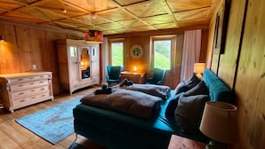 A wooden cabin bedroom with a bed, dresser, chair, and a small table with a lamp. - Double Room 'Zirben Nest' with Stunning View and Private Floor Bathroom (Hainzenberg)