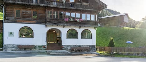 A traditional wooden building with balconies, arched windows, and a stone foundation.