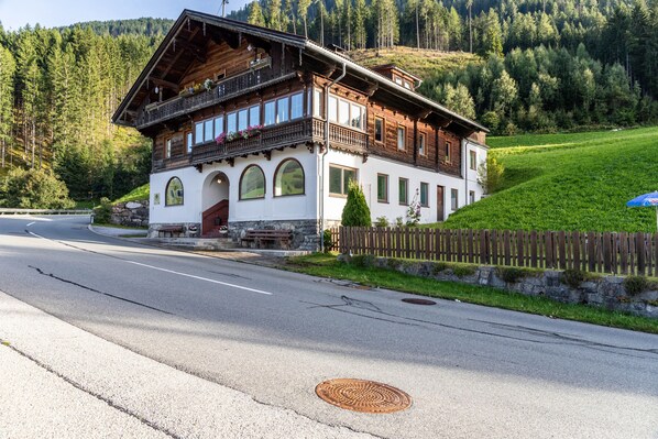Ein zweistöckiges Holzhaus mit Balkon, Rundbogenfenstern und einem Steinfundament.