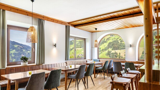 Un espace repas avec des tables et des chaises en bois, de grandes fenêtres donnant sur la campagne et un plafond en bois.