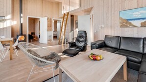 A modern interior with a wooden floor, a black leather sofa, a white chair, a wooden table with fruit, and a painting of a beach. - "Kanerva" -  from the sea by Interhome (Ulfborg)