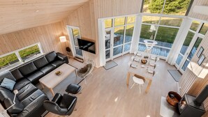 A spacious living area with a wooden ceiling, a black leather sofa, a dining table with chairs, and a fireplace. - "Kanerva" -  from the sea by Interhome (Ulfborg)