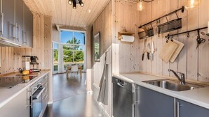 A modern kitchen with wooden walls, stainless steel appliances, and a view of the outdoors. - "Kanerva" -  from the sea by Interhome (Ulfborg)