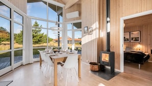 A modern interior with a dining area, a fireplace, and large windows offering a view of the outdoors. - "Kanerva" -  from the sea by Interhome (Ulfborg)
