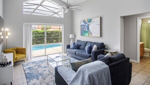 A spacious living room with a large window, a ceiling fan, a pool view, a modern sofa, and a yellow armchair. - 5BR,3BA Villa in Solana Resort,Pool,Near Disney (Davenport)